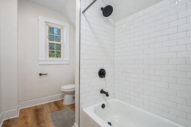 bathroom with toilet, wood-type flooring, vaulted ceiling, and tiled shower / bath