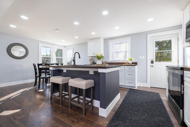 kitchen with white cabinets, stove, an island with sink, and dark hardwood / wood-style floors