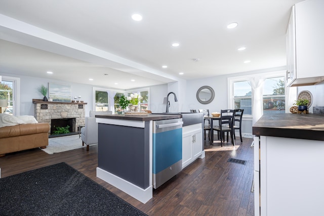 kitchen with white cabinets, a fireplace, dark wood-type flooring, a center island with sink, and dishwasher