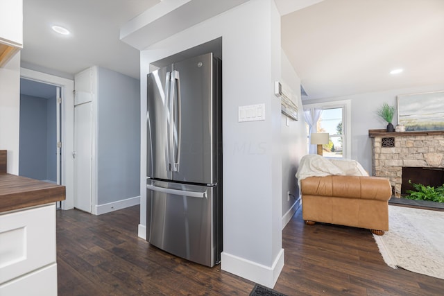 kitchen featuring stainless steel refrigerator, dark wood-type flooring, wood counters, a stone fireplace, and white cabinets