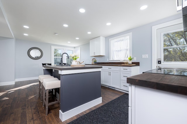 kitchen with a center island with sink, a kitchen breakfast bar, white cabinetry, and dark wood-type flooring