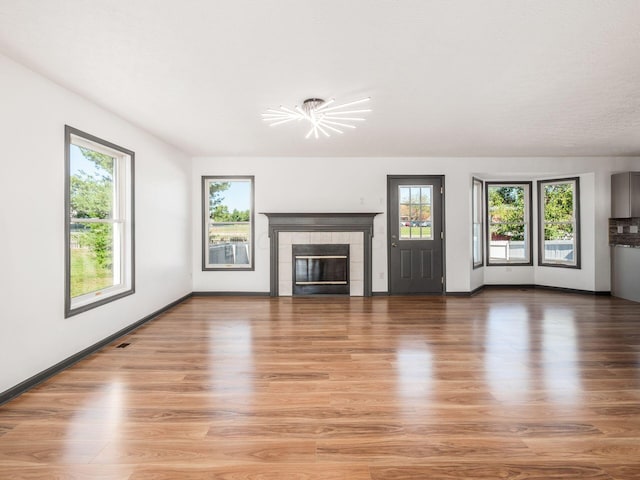 unfurnished living room with a tile fireplace, hardwood / wood-style floors, and plenty of natural light