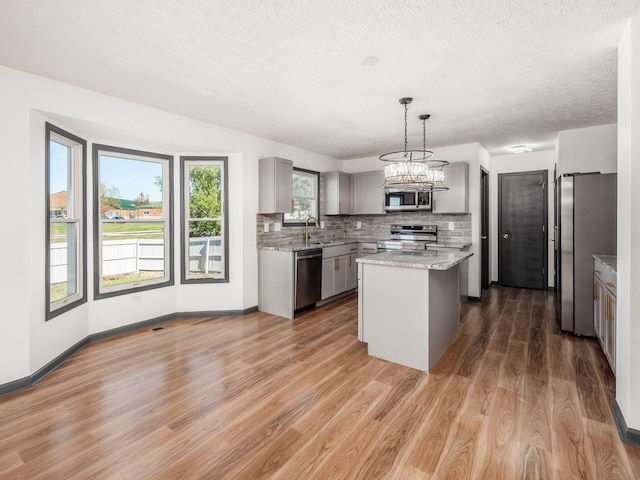 kitchen featuring hanging light fixtures, wood-type flooring, gray cabinets, a kitchen island, and appliances with stainless steel finishes