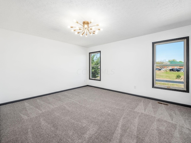 carpeted empty room with a textured ceiling and a chandelier