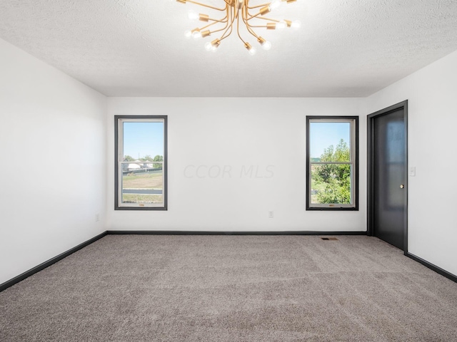 carpeted empty room featuring a textured ceiling and an inviting chandelier