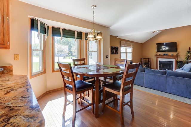 dining area featuring hardwood / wood-style floors, vaulted ceiling, and a tiled fireplace