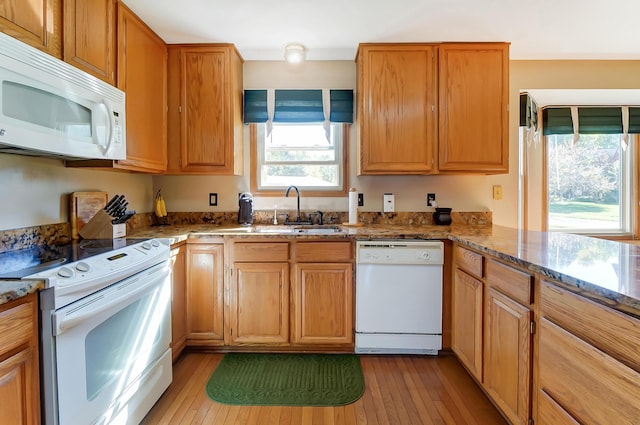 kitchen with light wood-type flooring, white appliances, stone counters, and sink