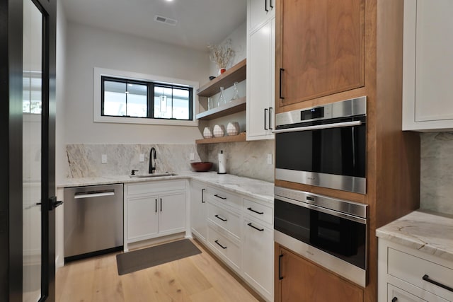 kitchen featuring appliances with stainless steel finishes, light stone counters, white cabinetry, and sink