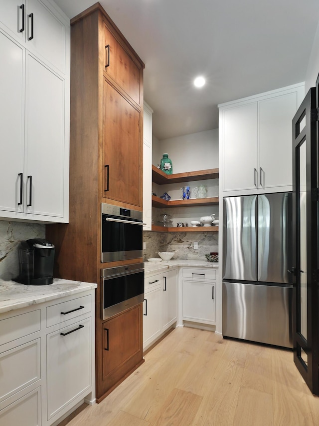 kitchen with tasteful backsplash, light stone counters, stainless steel appliances, light hardwood / wood-style flooring, and white cabinetry