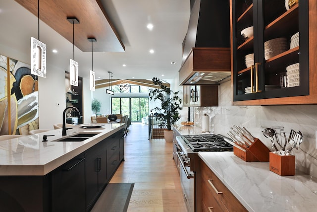 kitchen featuring custom exhaust hood, hanging light fixtures, sink, light hardwood / wood-style flooring, and stainless steel range