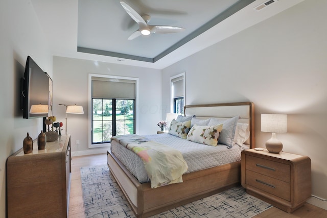 bedroom featuring a tray ceiling, light hardwood / wood-style flooring, and ceiling fan