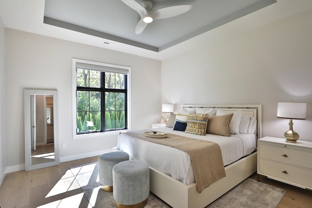 bedroom with a tray ceiling, ceiling fan, and light hardwood / wood-style floors