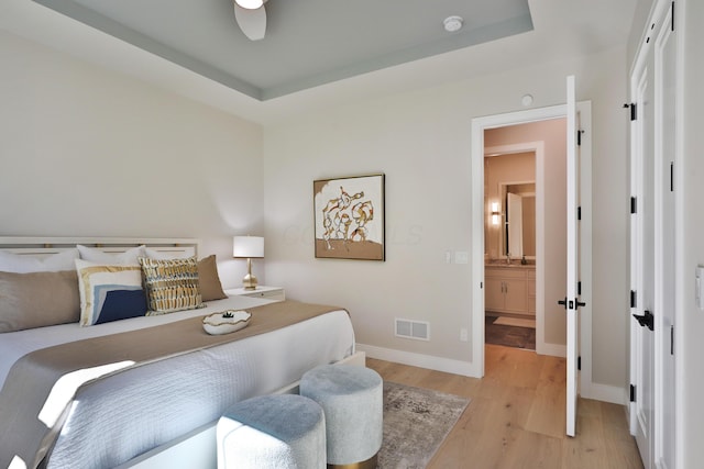 bedroom featuring a raised ceiling, ceiling fan, and light wood-type flooring