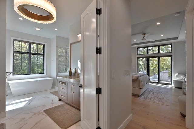 bathroom featuring a bathing tub, ceiling fan, wood-type flooring, a tray ceiling, and vanity