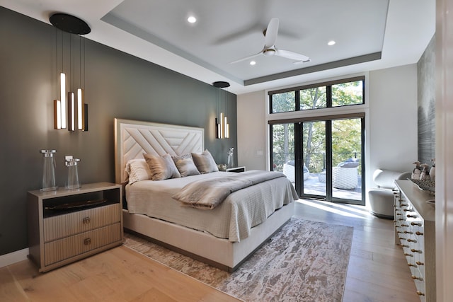 bedroom with access to exterior, a tray ceiling, light hardwood / wood-style flooring, and ceiling fan