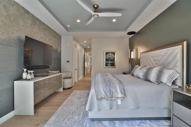 bedroom with a tray ceiling, ceiling fan, and light hardwood / wood-style flooring