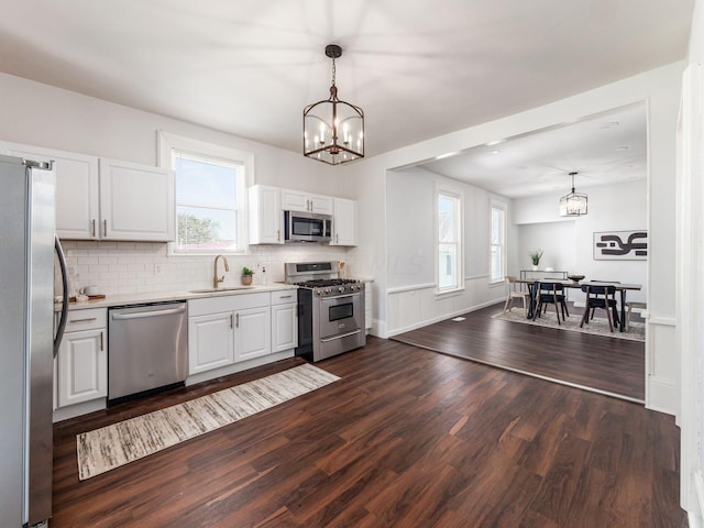 kitchen featuring stainless steel appliances, white cabinetry, hanging light fixtures, and dark hardwood / wood-style floors