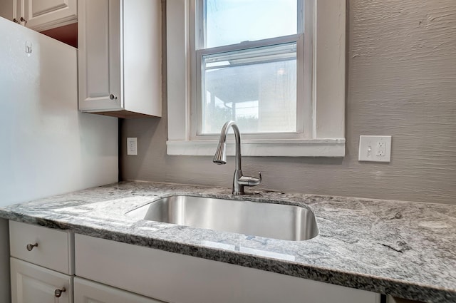 kitchen featuring white cabinetry, sink, and light stone countertops