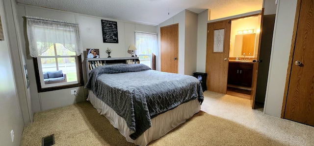 bedroom with light colored carpet, lofted ceiling, a textured ceiling, and ensuite bath