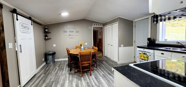 dining space with sink, a barn door, ornamental molding, lofted ceiling, and light wood-type flooring