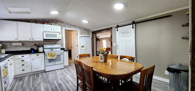 kitchen featuring white appliances, vaulted ceiling, a barn door, light hardwood / wood-style floors, and white cabinetry