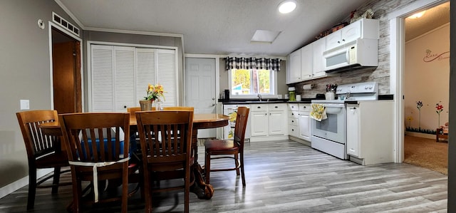 kitchen with white appliances, white cabinets, sink, a textured ceiling, and light hardwood / wood-style floors