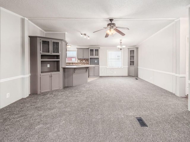 unfurnished living room featuring ceiling fan with notable chandelier, a textured ceiling, carpet floors, and crown molding