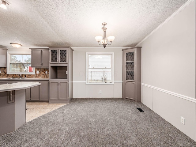 kitchen with sink, a notable chandelier, light colored carpet, decorative backsplash, and ornamental molding