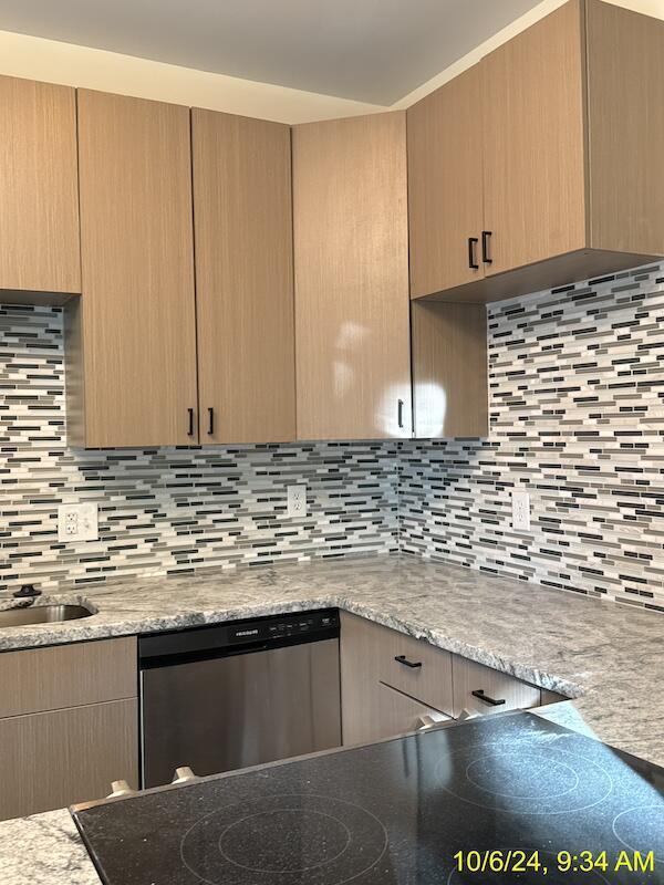 kitchen featuring backsplash, light brown cabinetry, light stone counters, and dishwasher