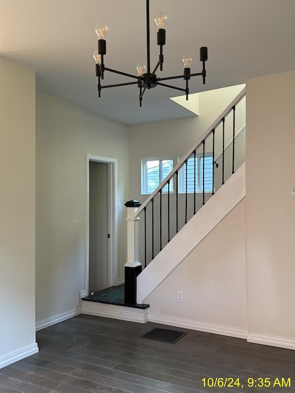 staircase with wood-type flooring and an inviting chandelier