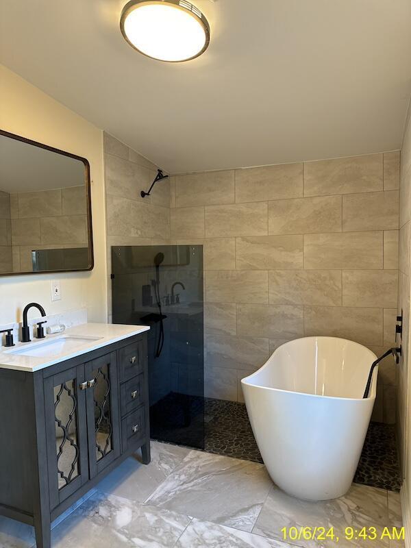 bathroom with vanity, independent shower and bath, and tile walls