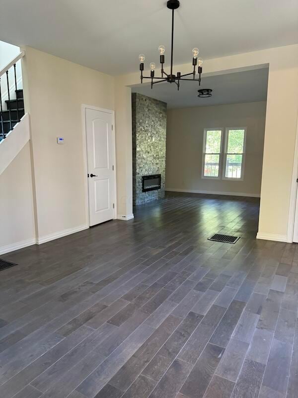 unfurnished living room featuring a stone fireplace, dark hardwood / wood-style flooring, and a chandelier