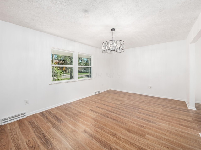 empty room with a textured ceiling, light wood-type flooring, and an inviting chandelier