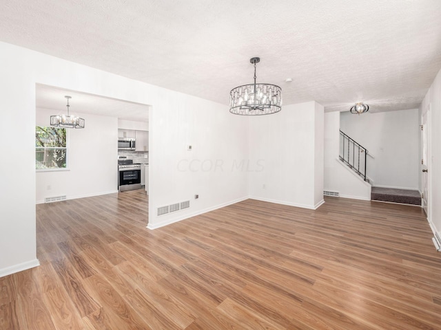 unfurnished living room featuring wood-type flooring, a textured ceiling, and a notable chandelier