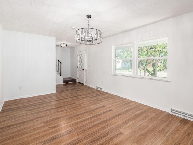 unfurnished room featuring wood-type flooring, a textured ceiling, and an inviting chandelier