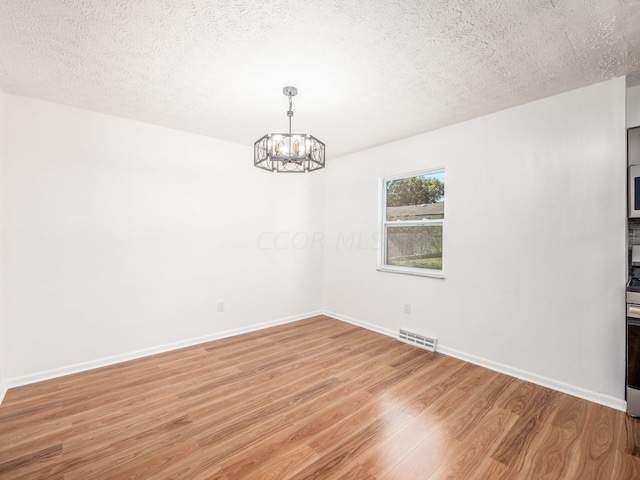 unfurnished room featuring a notable chandelier, light wood-type flooring, and a textured ceiling