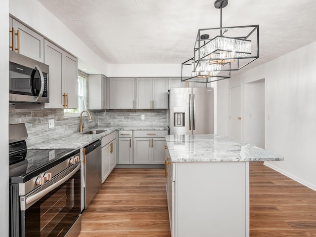 kitchen with sink, gray cabinets, light wood-type flooring, a kitchen island, and stainless steel appliances