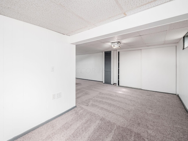 basement featuring a paneled ceiling and light carpet