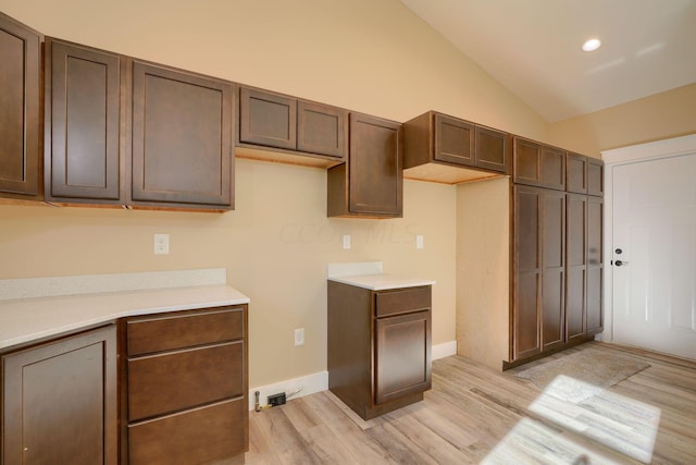 kitchen with dark brown cabinetry, light hardwood / wood-style flooring, and vaulted ceiling