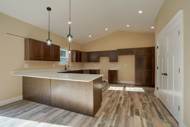 kitchen with sink, hanging light fixtures, kitchen peninsula, vaulted ceiling, and light wood-type flooring