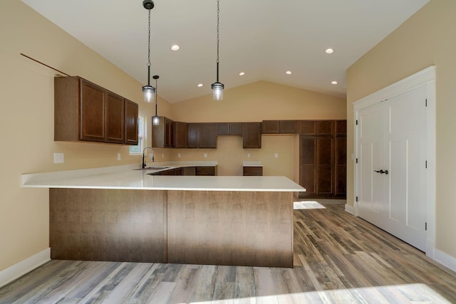 kitchen featuring lofted ceiling, sink, light hardwood / wood-style flooring, decorative light fixtures, and kitchen peninsula