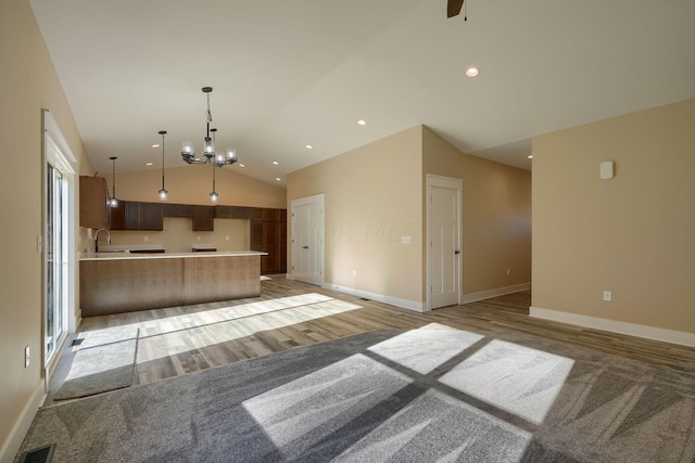 kitchen with pendant lighting, sink, vaulted ceiling, light hardwood / wood-style floors, and a chandelier