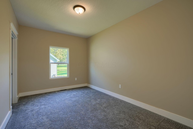 unfurnished room with a textured ceiling and dark carpet