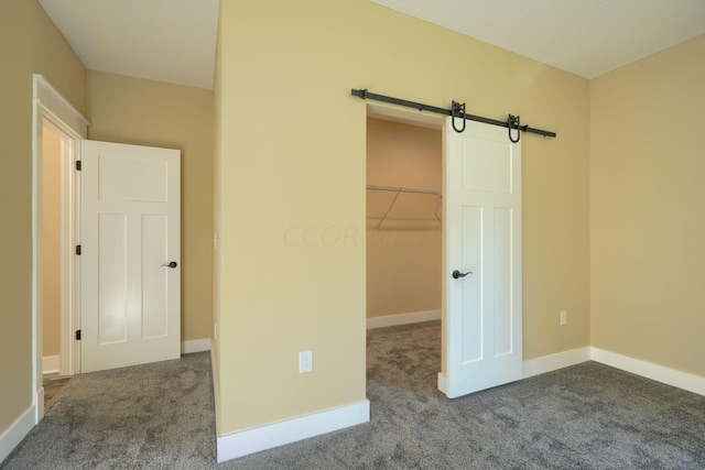 unfurnished bedroom with a barn door, a walk in closet, a closet, and carpet