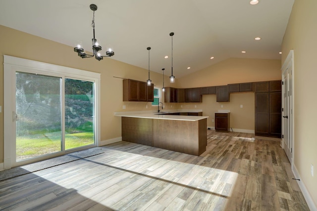 kitchen featuring kitchen peninsula, vaulted ceiling, sink, an inviting chandelier, and light hardwood / wood-style floors