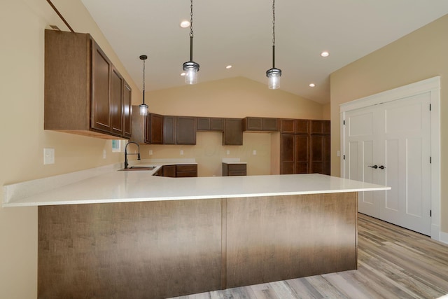 kitchen with light wood-type flooring, vaulted ceiling, hanging light fixtures, and sink