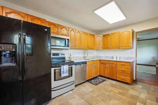 kitchen with light stone countertops, appliances with stainless steel finishes, light hardwood / wood-style floors, and sink