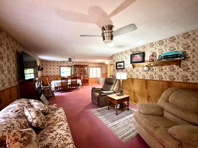 living room featuring carpet, wood walls, ceiling fan, and a textured ceiling