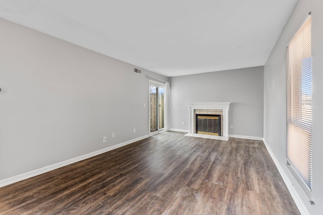 unfurnished living room with a tile fireplace and dark wood-type flooring