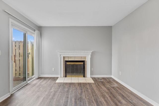 unfurnished living room with wood-type flooring and a tiled fireplace